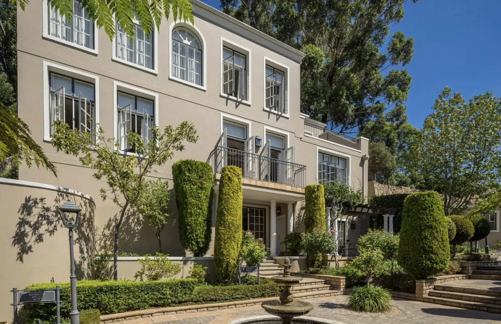 Four Seasons Hotel The Westcliff, Johannesburg: beige mansion with arched windows, balcony, manicured gardens, fountain on sunny hillside.