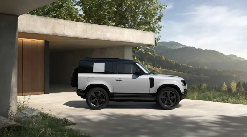 White Land Rover Defender SUV parked under modern carport with mountains and trees in background