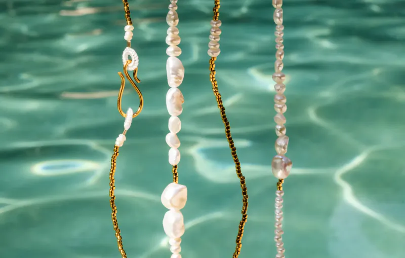 Pebble & Loop pearl necklaces with gold chains on turquoise water background