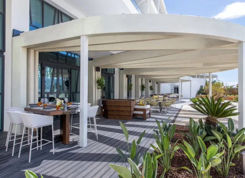 Outdoor terrace at W Algarve Hotel with white lounge chairs, wooden tables set for dining, plants, and ocean view.
