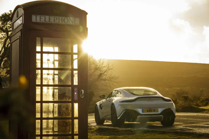 Silver Aston Martin Vantage parked beside classic red 'TELEPHONE' booth at sunset on North Coast 500 route