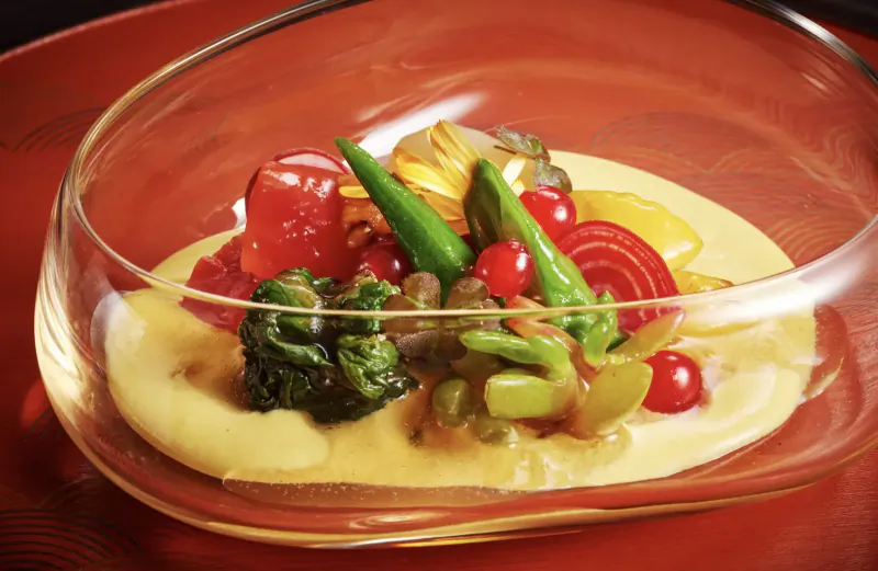 Kaiseki dish in curved glass bowl on red tray: vibrant broccoli, peppers, beets, beans on yellow sauce