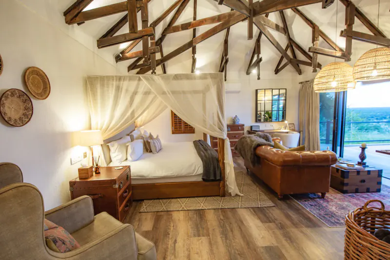 Luxurious Namibian safari lodge bedroom with canopy bed, leather sofa, open doors to savanna vista