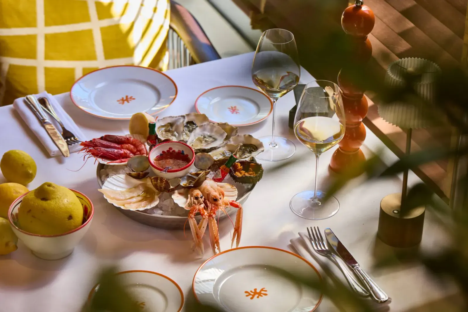 Elegant seafood platter with oysters, prawns, shrimp on white plates with 'ALBA' logo, wine glasses, lemons on table