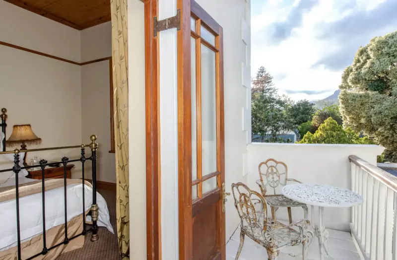 Elegant bedroom with brass bed opening to balcony with ornate chairs, table, and Stellenbosch mountain view.