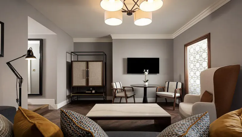 Elegant Parkgate Hotel living room with gray walls, chandelier, armchairs, coffee table, TV, and vase.