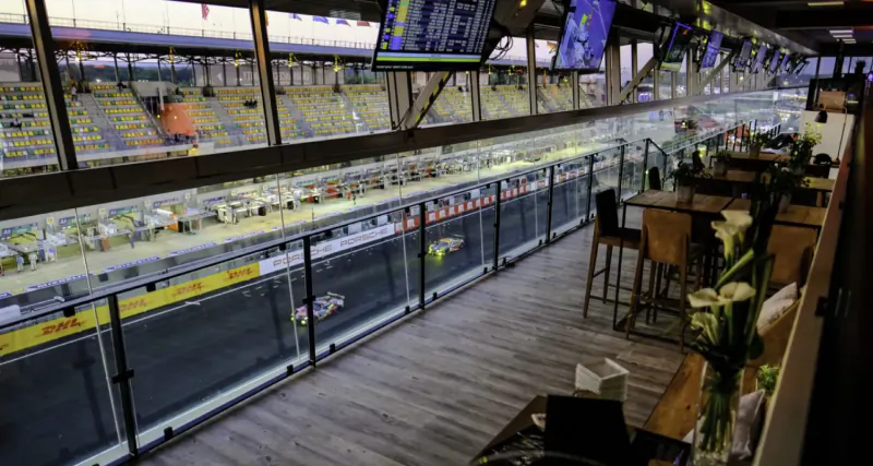 Le Jardin Privé private lounge overlooking Le Mans 24hr racetrack with cars racing, tables, chairs, and flowers.