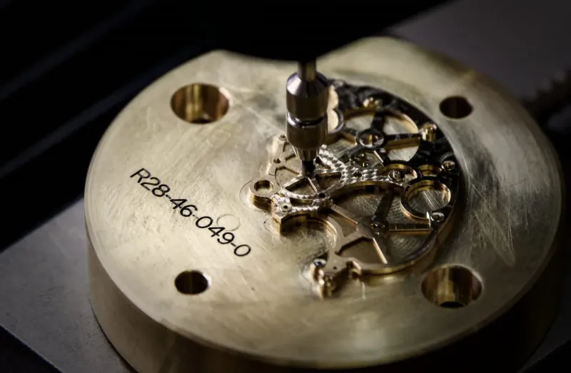 Close-up of gold BOVET watch movement R28-460490 being drilled, intricate gears visible on brass plate