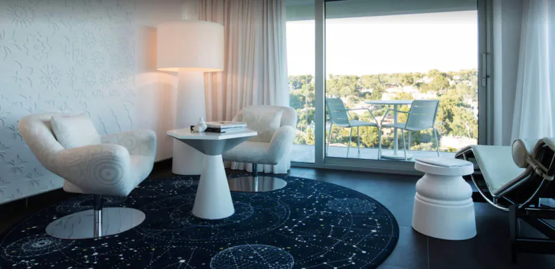 Marcel Wanders' iconic white modern lounge in Grand Hotel Portals Nous with starry rug, overlooking tropical view.