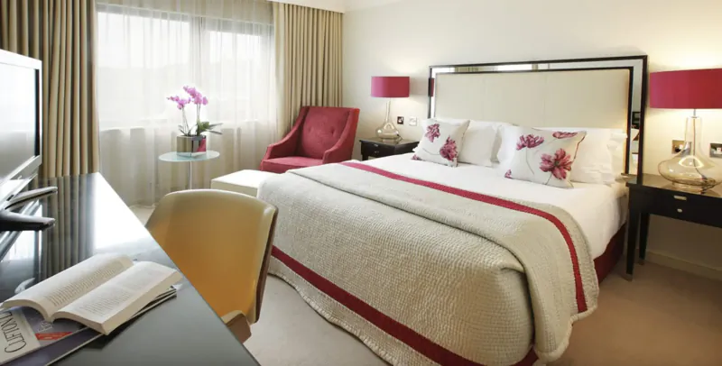 Elegant hotel room at The Bristol with king bed, red pillows, orchids, desk, and armchairs.