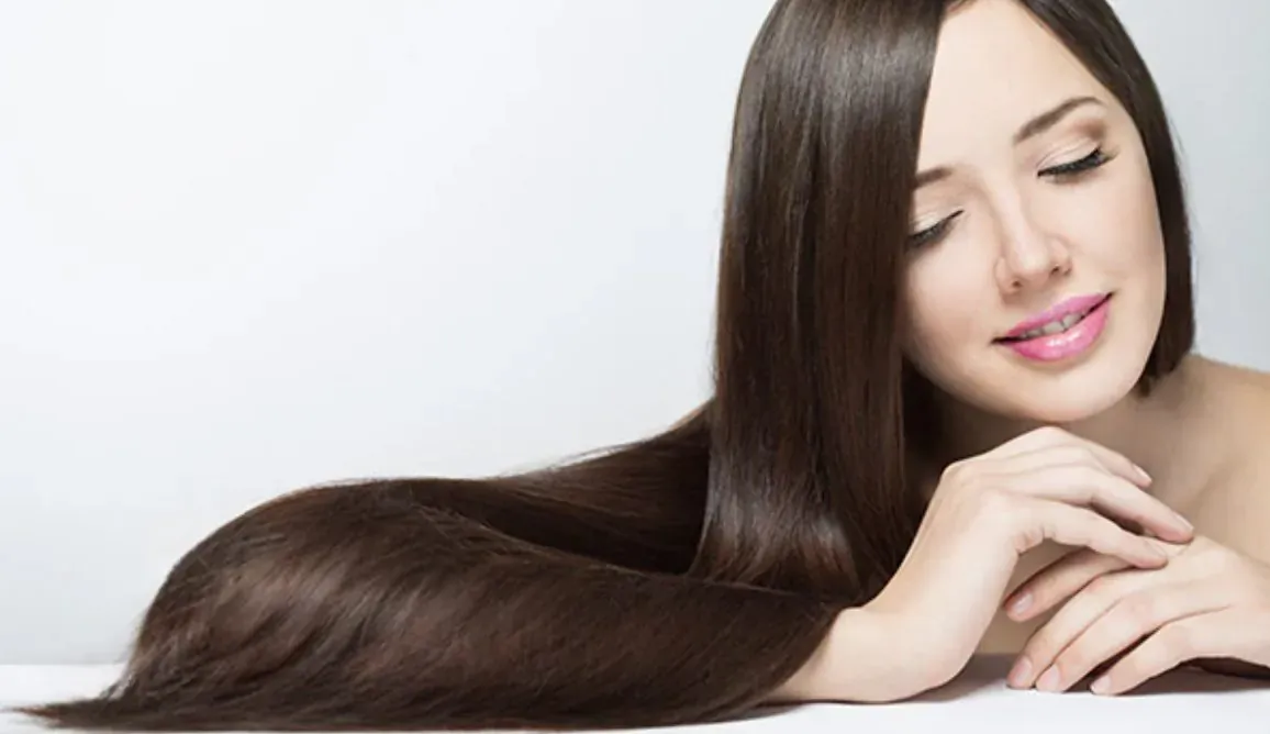 Close-up of woman with long straight brown hair, eyes closed, smiling softly on white background