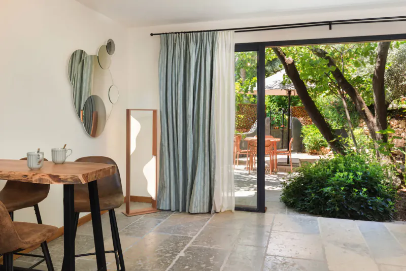 Modern interior with wooden table, chairs, abstract wall art, and sliding doors to lush green garden patio.