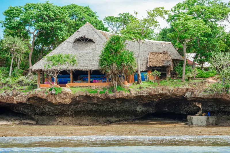 Traditional thatched Kenyan beach hut on cliff overlooking sandy shore and ocean, Kisite-Mpunguti Marine Park