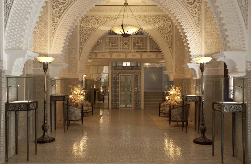 Opulent arched lobby of Royal Mansour Marrakech medina with ornate white plasterwork, pendant lamps, plush chairs, and pedestals.