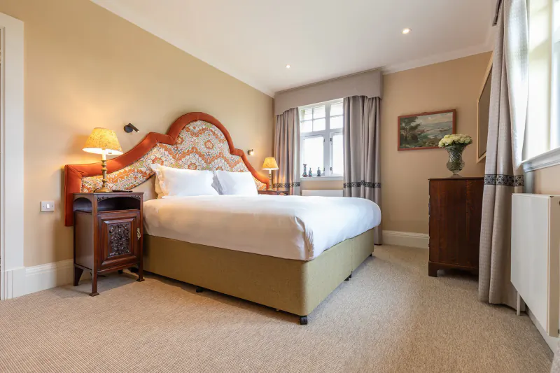 Luxury bedroom in Fairmont St Andrews Manor Home with ornate orange headboard, white bed, wall lamps, and window view.