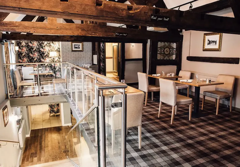 Elegant dining area in Cheshire Manor House Hotel with wooden beams, glass balcony overlooking tables and chairs.