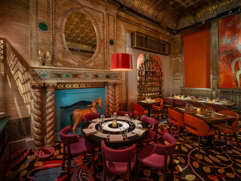 Opulent Masala Zone brasserie interior with turquoise carousel horse by ornate fireplace, red lamps, lazy Susan table, and orange chairs.