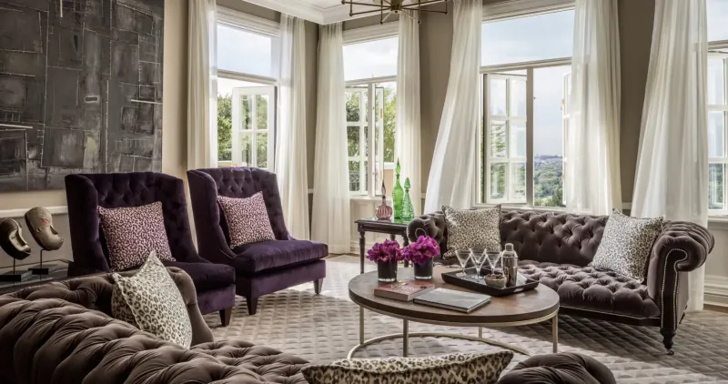 Elegant living room at Four Seasons Westcliff above Johannesburg with purple armchairs, tufted sofa, flowers, and city view through large windows.
