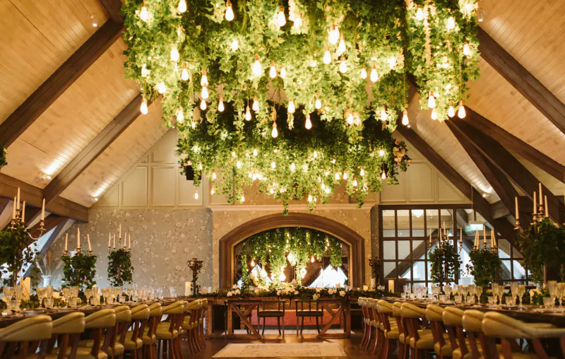 Elegant wedding venue at The Rabbit Hotel with lush green floral chandelier over long wooden dining tables.