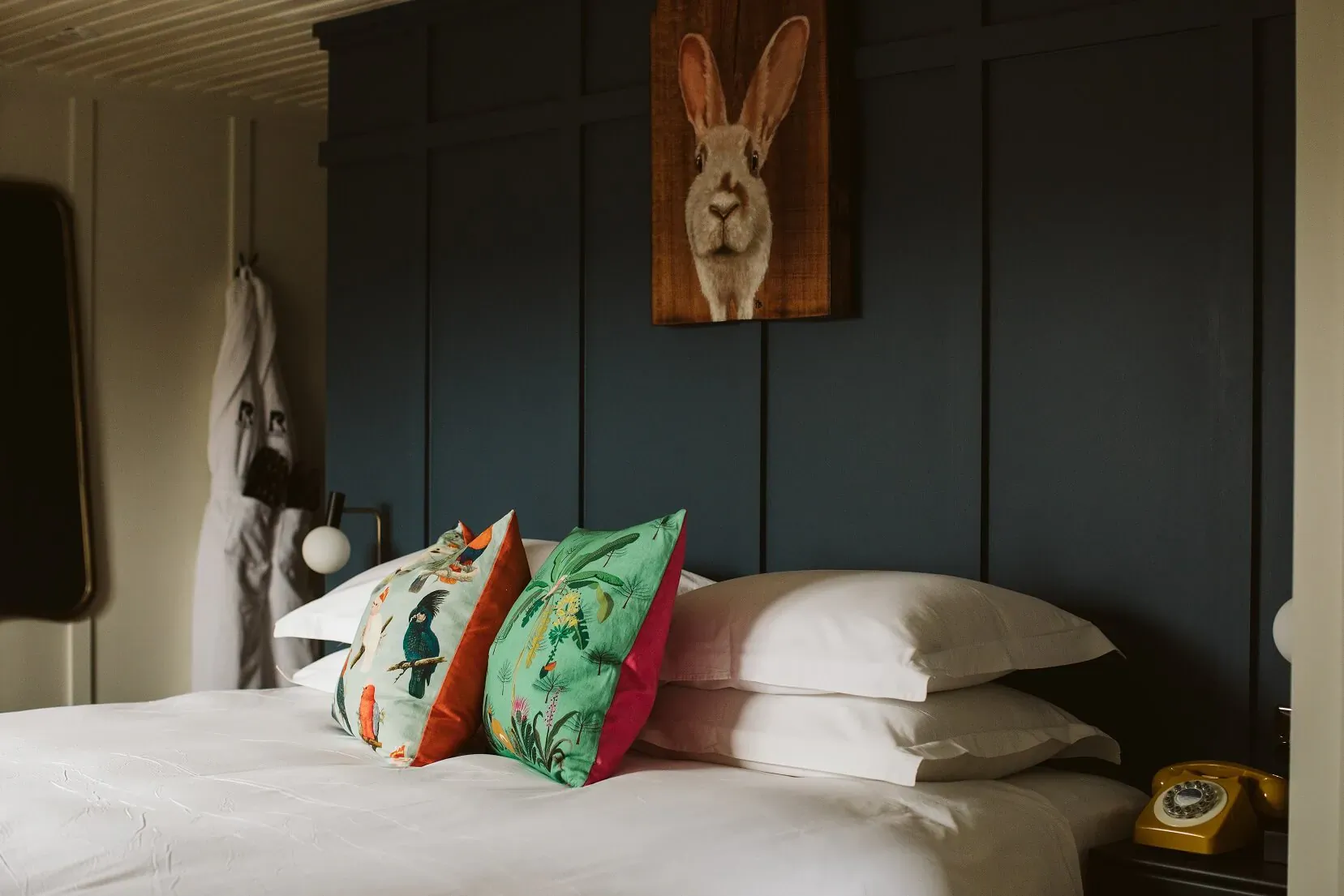 Cozy bed at The Rabbit Hotel with rabbit art on navy wall, floral pillows, vintage rotary phone, and hanging towel.