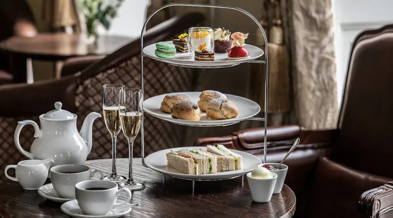 Elegant afternoon tea at Bailbrook House Hotel: tiered stand with sandwiches, scones, cakes, teapot, cups, and champagne flutes on table.