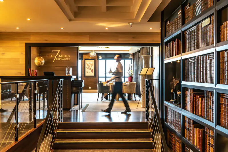 Man walking down stairs in Hotel Tides lobby with wooden bookshelves, warm lighting, and globe sign.