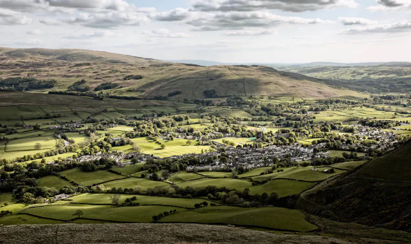 Aerial view of lush green valleys, rolling hills, and a small village under partly cloudy skies