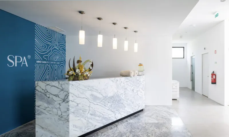 Modern SPA reception desk with marble counter, blue wavy wall, floral arrangement, pendant lights, and hallway