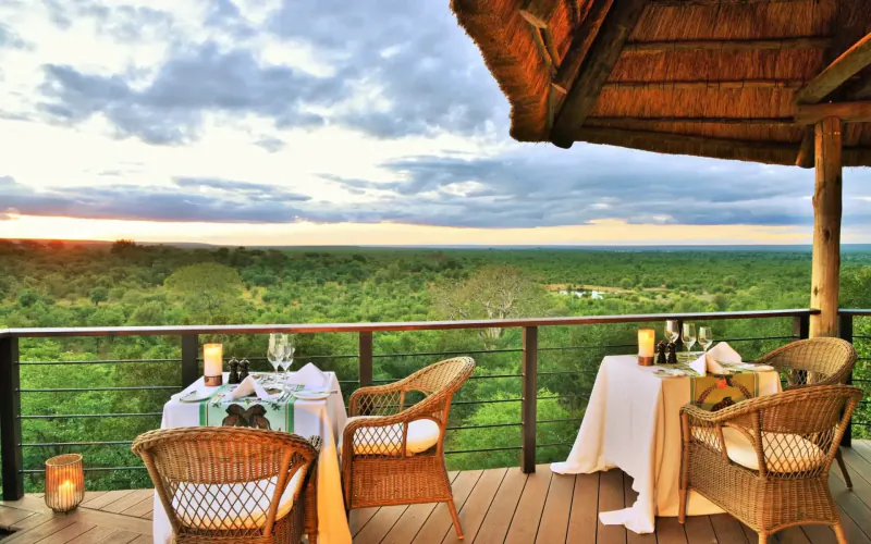 Romantic candlelit dinner on a thatched deck overlooking Victoria Falls savanna at sunset.