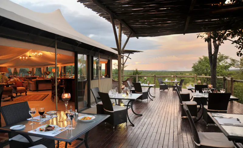 Luxury canvas lodge deck at Elephant Camp with candlelit dining tables, sunset savanna view from Zimbabwe.