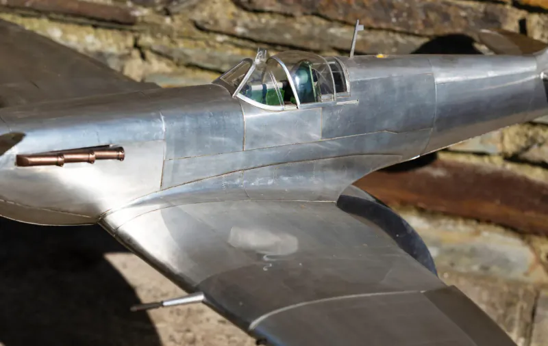 Detailed scale model of silver Supermarine Spitfire fighter plane on stone wall backdrop