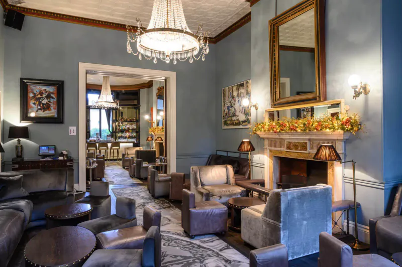 Festive lounge at Home House, London: chandelier-lit seating area with autumn garland above fireplace, blue walls, art.
