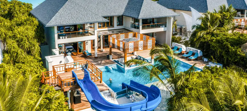 Aerial view of Hideaway Beach Resort & Spa: luxury villas, blue pool with waterslide, surrounded by tropical greenery.