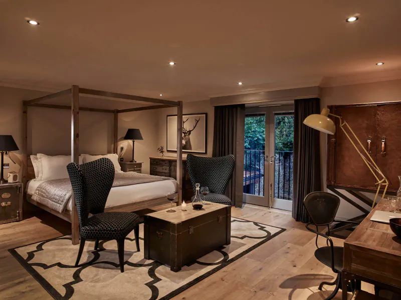 Elegant bedroom in Harper Norfolk with wooden four-poster bed, velvet chairs, brass lamps, and balcony doors to garden.