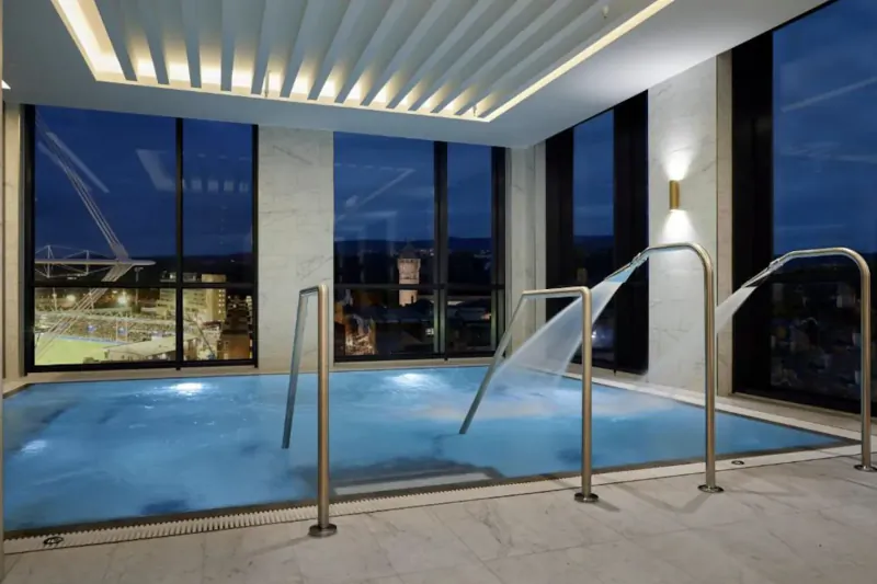 Luxurious indoor pool at The Parkgate Hotel Cardiff at night, with glowing blue water, chrome handrails, and city skyline view through large windows.