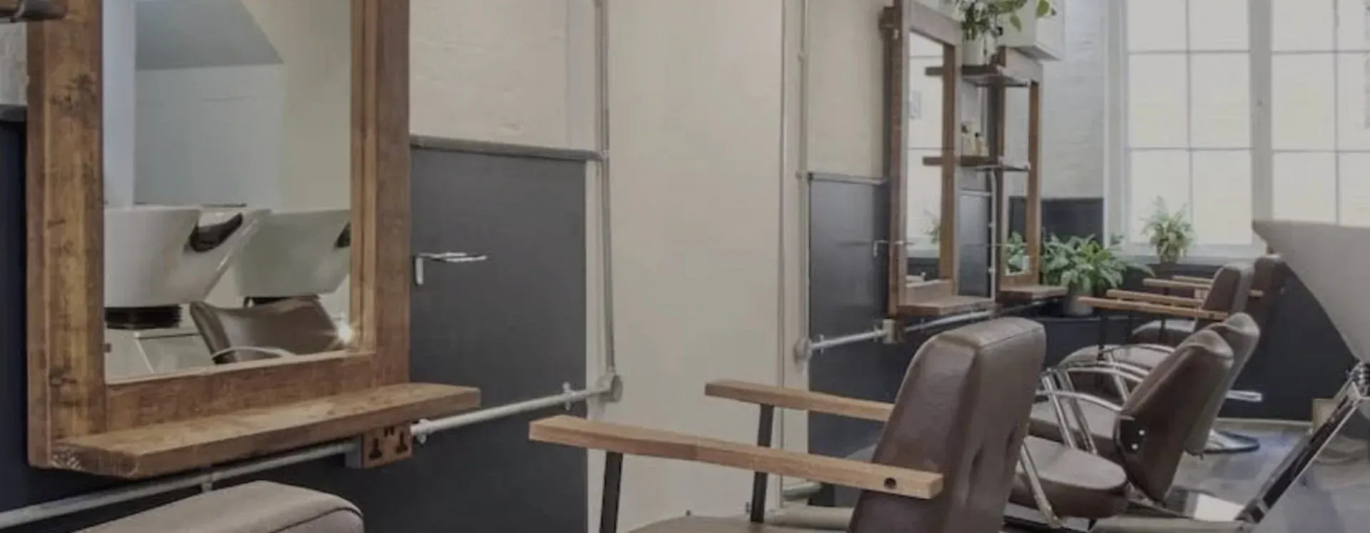 Modern empty hair salon with wooden-framed mirrors, leather chairs, plants, and large windows