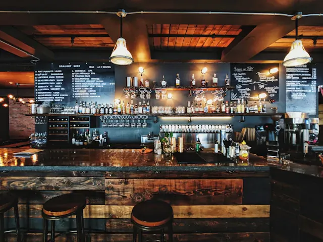 Rustic wooden bar counter in Philadelphia with blackboard menus, liquor shelves, pendant lights, and barstools.