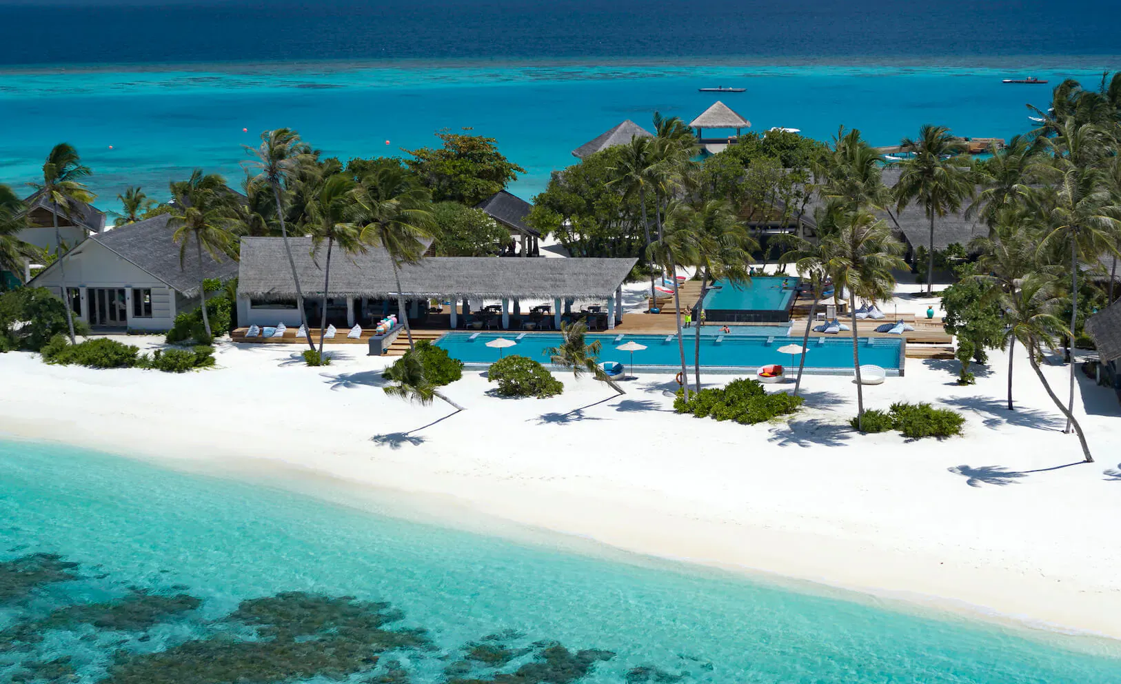 Aerial view of Cora Cora Maldives resort with thatched villas, infinity pool, white sand beach, and turquoise lagoon.