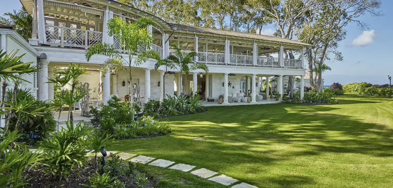 White tropical villa with verandas, surrounded by lush palms and manicured lawn under blue sky