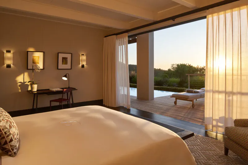 Luxurious bedroom at Delaire Graff Estate with open doors to sunset-view infinity pool in Cape Winelands