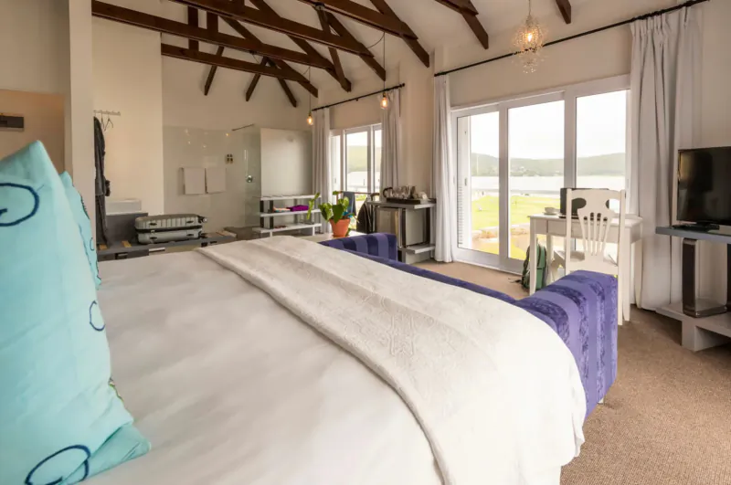 Spacious loft bedroom at The Lofts Boutique Hotel with white bed, purple ottoman, lake lagoon view through doors.