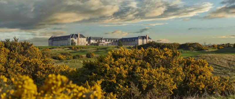 Large white manor house on grassy gorse-covered hills under dramatic cloudy sunset sky