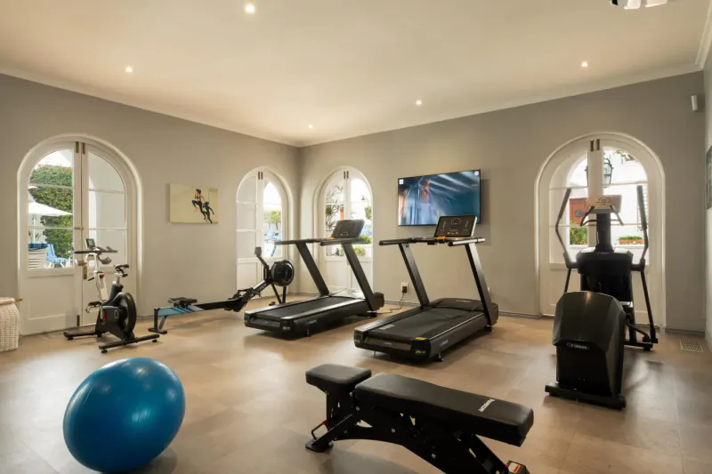 Modern hotel gym with treadmills, exercise bikes, weight bench, blue stability ball, and arched windows.