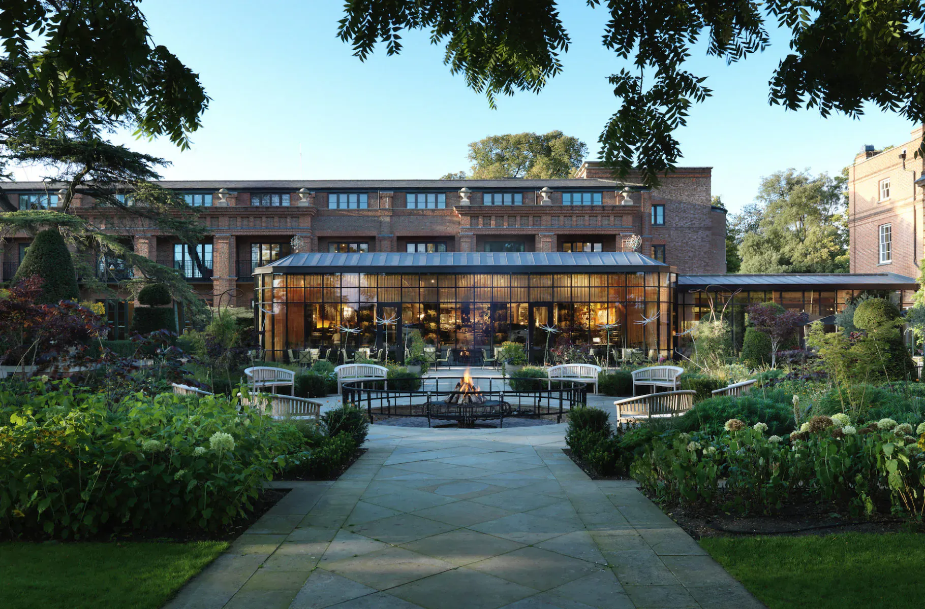 Glasshouse at The Grove: glazed extension with garden courtyard, fire pit, and lush plantings under trees.