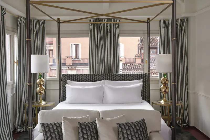 Elegant canopy bed with gray patterned headboard and pillows in luxurious Violino d'Oro Hotel room, Venice view.