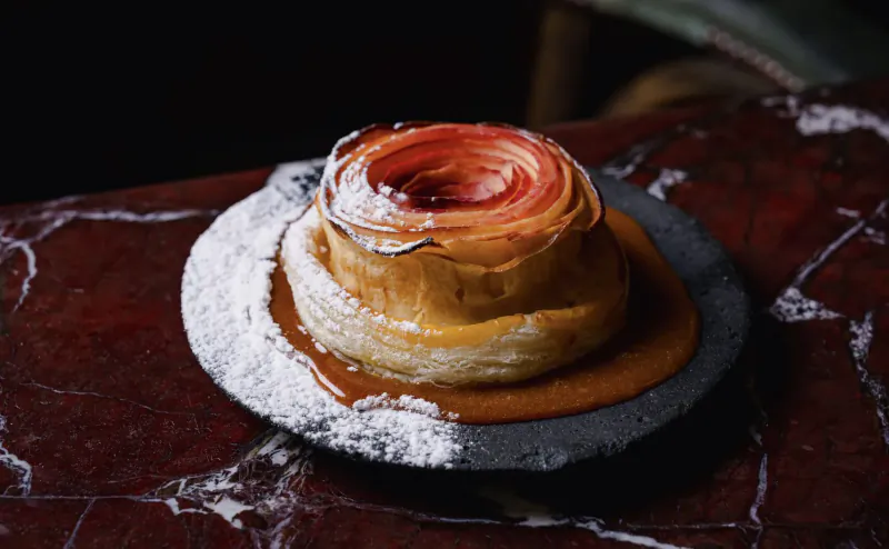 Close-up of swirled caramelized custard tart dusted with powdered sugar on a slate plate over red marble surface