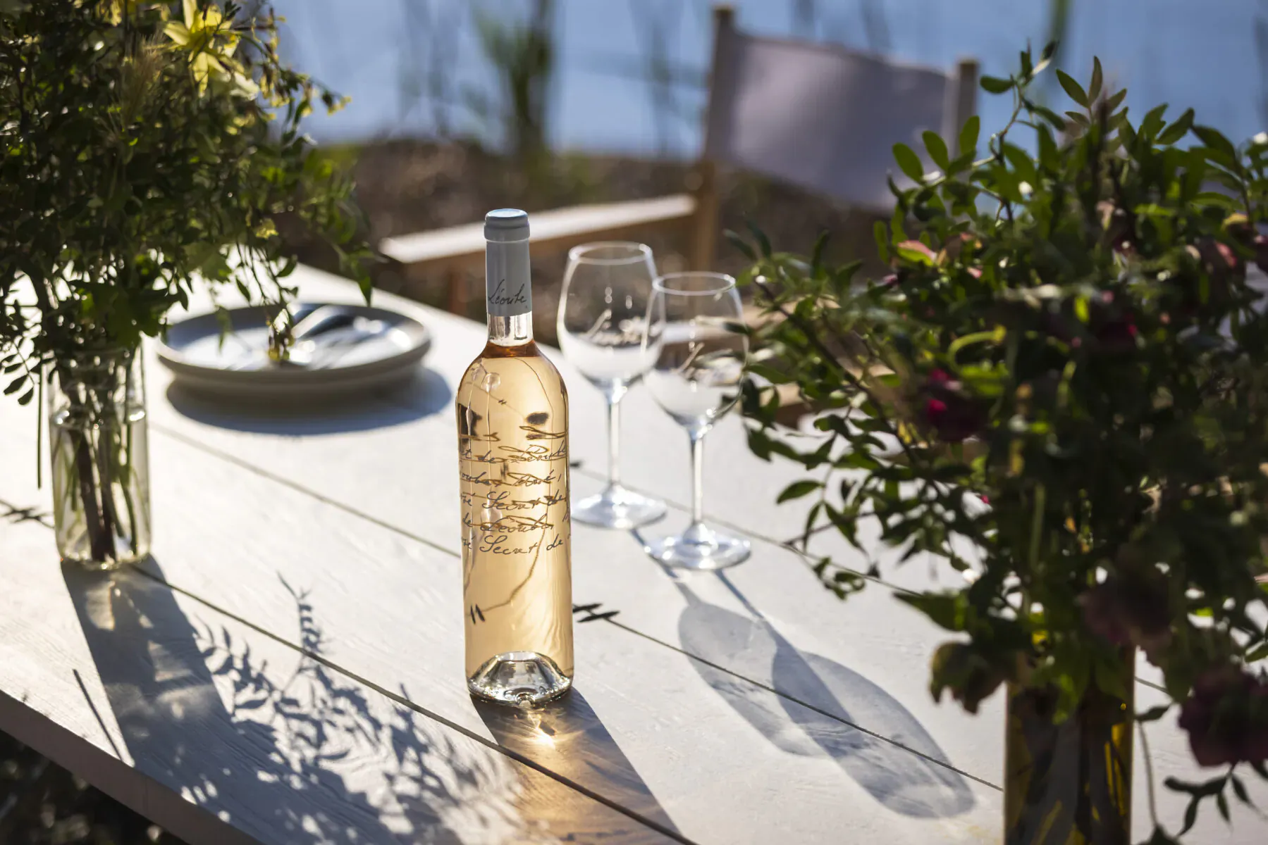 Château Léoube rosé wine bottle on wooden table with wine glasses, flowers, by lake at Château Léoube partnership event