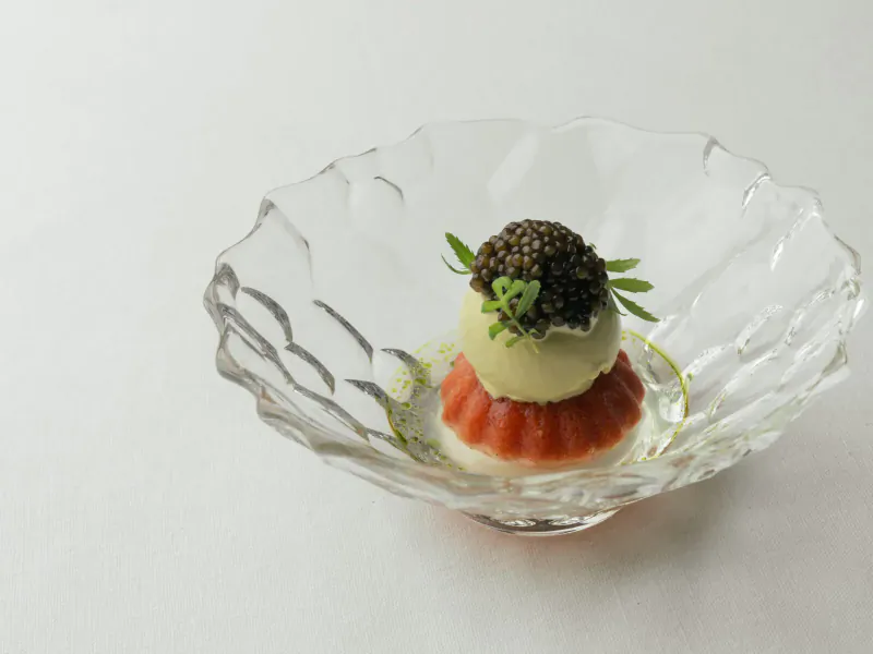 Elegant dish in clear bowl: tomato jelly base, pale cream mound topped with caviar and herb sprig.