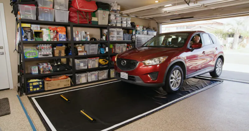 Red Mazda CX-5 on black GaraMat containment mat in garage with shelves of storage bins