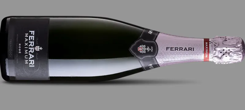 Ferrari Maximum Brut sparkling wine bottle with gold label and pink foil on gray background